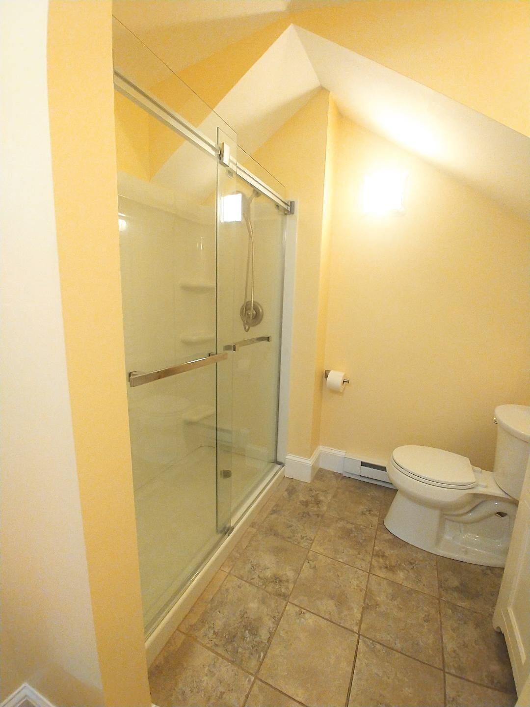 A bathroom with a glass shower enclosure, a toilet, and a tiled floor.