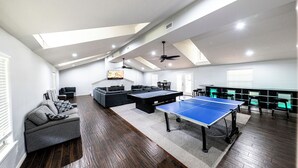 Uma sala de estar ampla com mesa de pingue-pongue, sofá e ventoinha no teto.