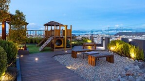 A wooden play structure with a slide, surrounded by a landscaped garden with gravel paths and benches.