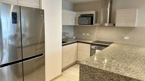 A modern kitchen with stainless steel appliances, granite countertops, and light wood cabinetry.