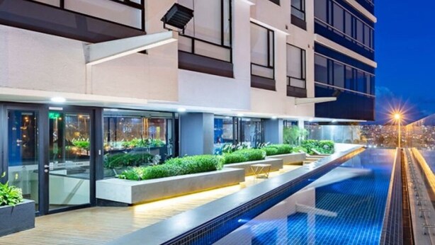 A modern hotel with a swimming pool, glass doors, and a city view at night.