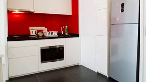 A modern kitchen with white cabinets, a red accent wall, a black countertop, and a built-in oven.