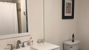 A bathroom with a white sink, two faucets, a mirror, a toilet, and a framed picture on the wall. - Relaxed and Spacious 2 BR Apartment with a Patio (Oakland)