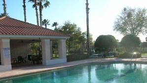 A swimming pool with a covered area, palm trees, and a clear sky. - Private Oasis Near Disney | Golf Course Home with Private Pool | Pet Friendly (Davenport)
