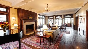 Un salón amplio con un piano de cola, una chimenea y un ventanal grande.
