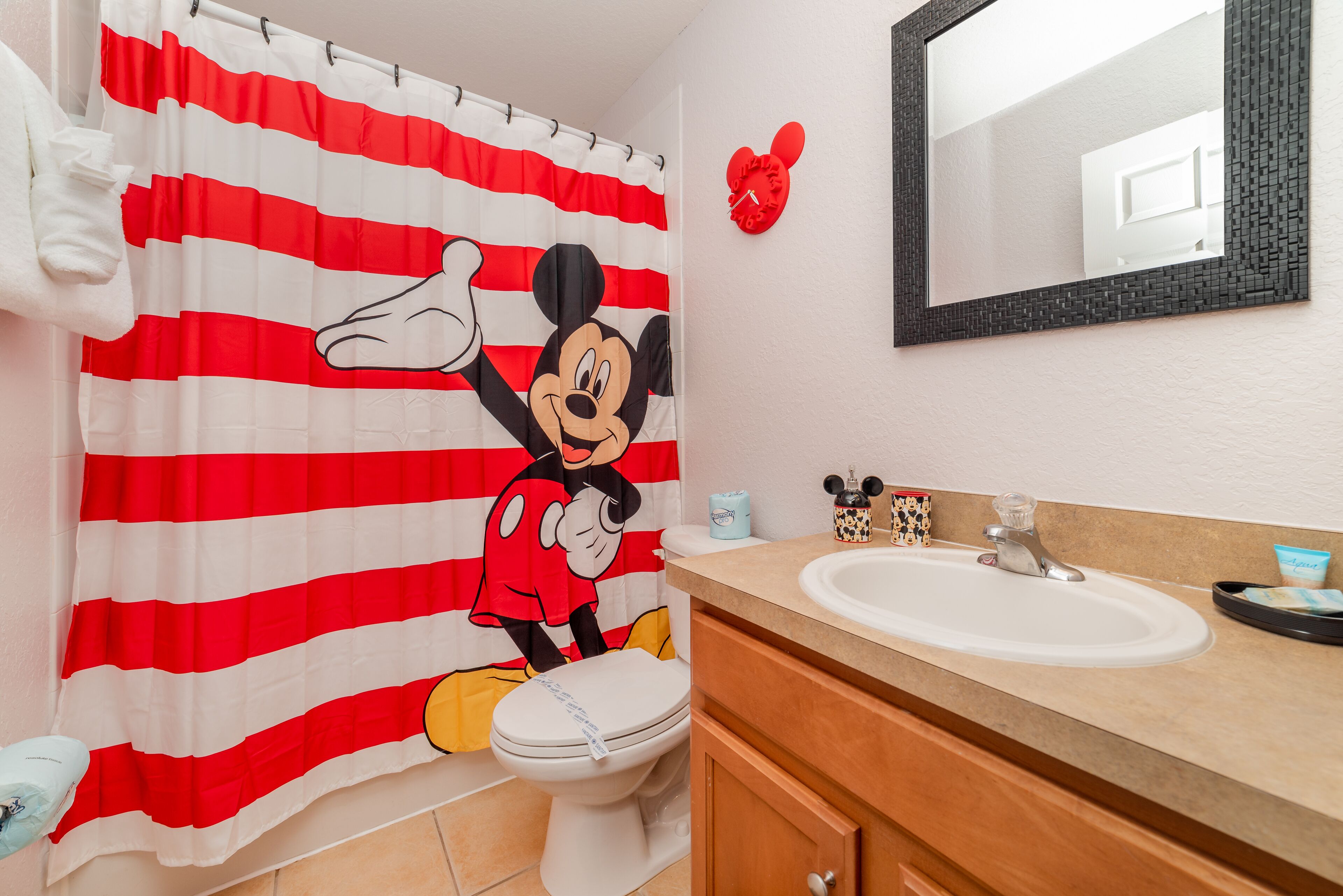 Ein Badezimmer mit Duschvorhang mit Mickey Mouse Motiv, einem Waschbecken und einem Spiegel.