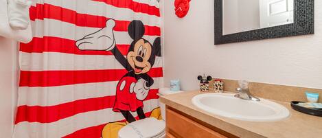 Ein Badezimmer mit Duschvorhang mit Mickey Mouse Motiv, einem Waschbecken und einem Spiegel.