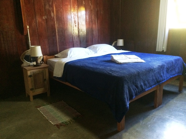 A bedroom with a wooden bed, a nightstand with a lamp, and a window with curtains.