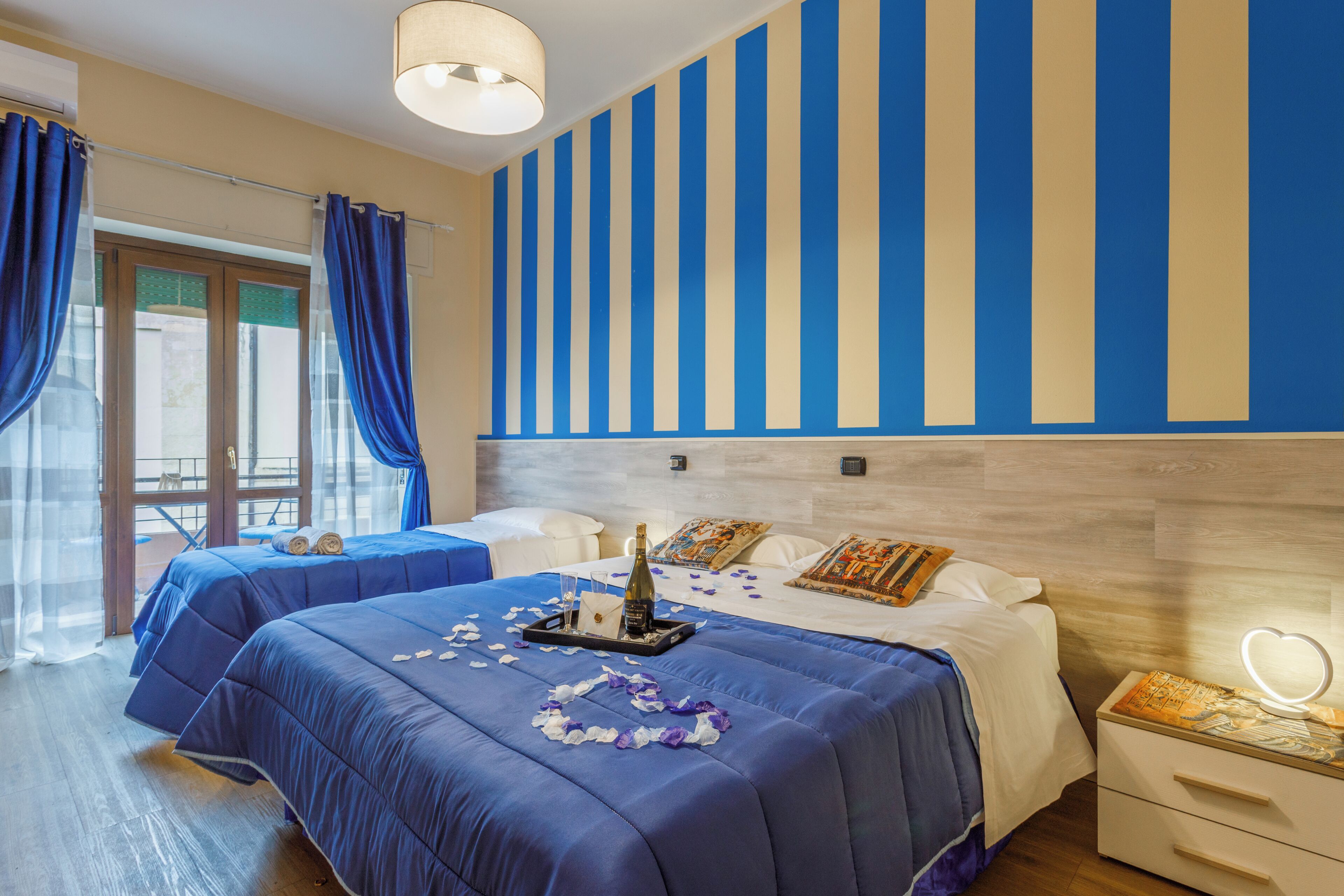 Habitación de hotel con dos camas, un ventanal con cortinas, un minibar y un adornado en la pared.