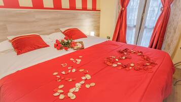 A bed with red bedding, a bouquet of flowers, and scattered rose petals.