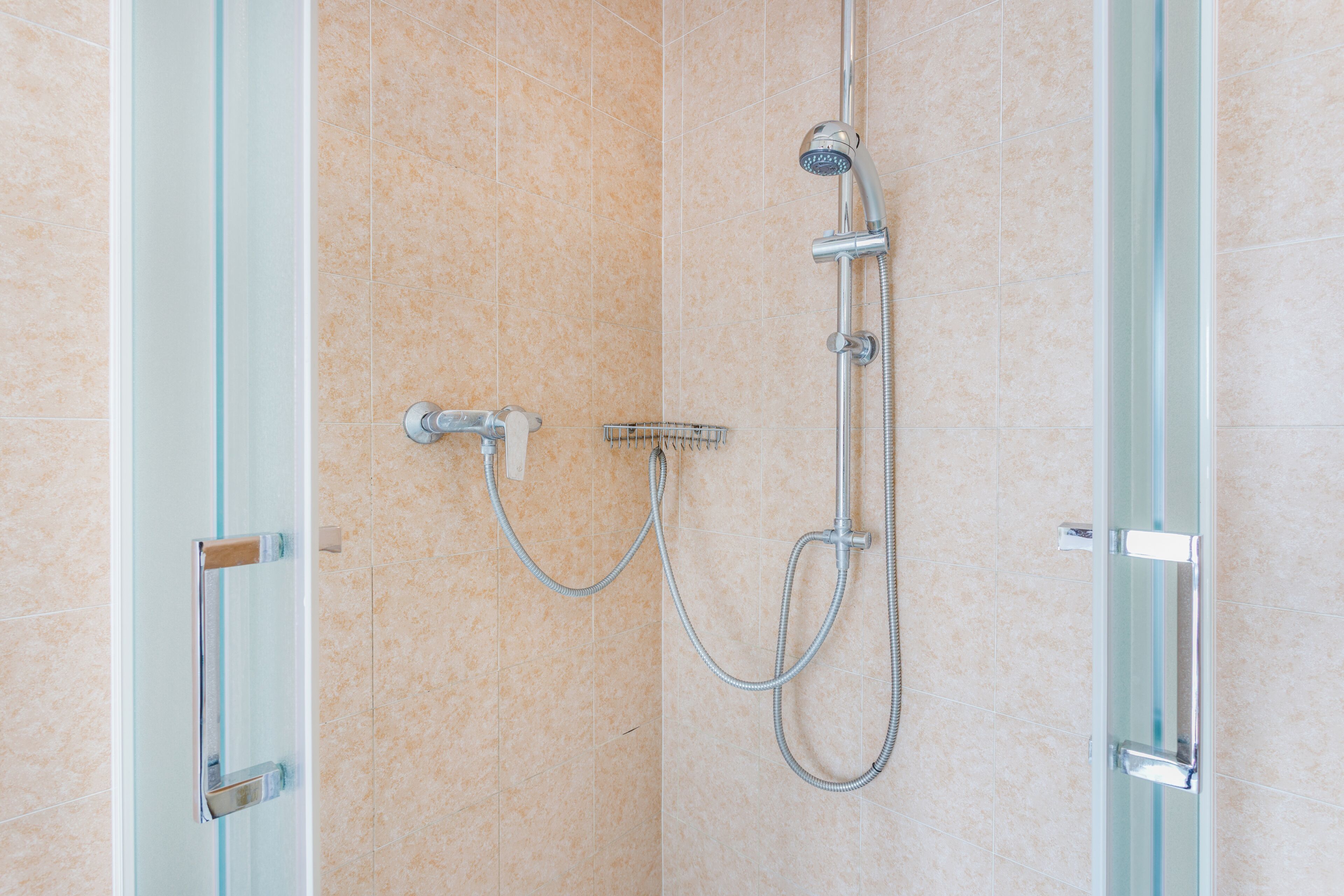A shower with a handheld showerhead, a wall-mounted faucet, and a handheld showerhead.