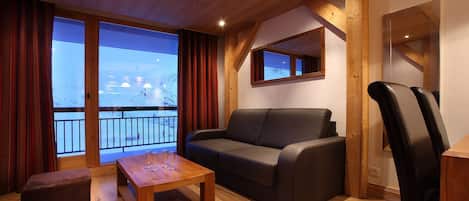 Una sala de estar acogedora con techo de madera, un sofá de cuero oscuro, una mesa de centro de madera y un ventanal con cortinas.