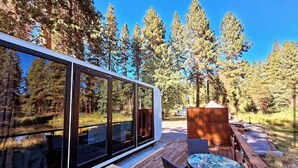 A modern outdoor deck with a glass enclosure, wooden furniture, and a view of a forested area. - Crater Lake Resort (Chiloquin)