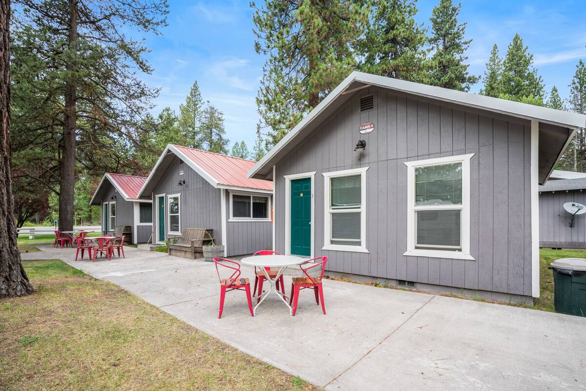 A row of cabins with a concrete patio, red chairs, and a green door.