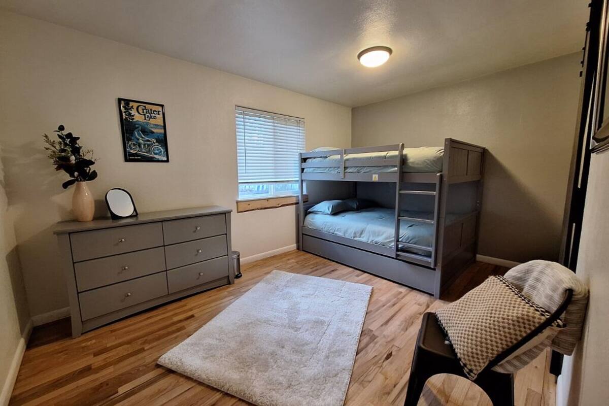 A compact room with a bunk bed, a dresser, a small rug, and a window with blinds.