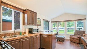 A kitchen with dark wood cabinets, a granite countertop, and a gas stove. There is a large window with blinds, a microwave, and a sink. - Crater Lake Resort (Chiloquin)