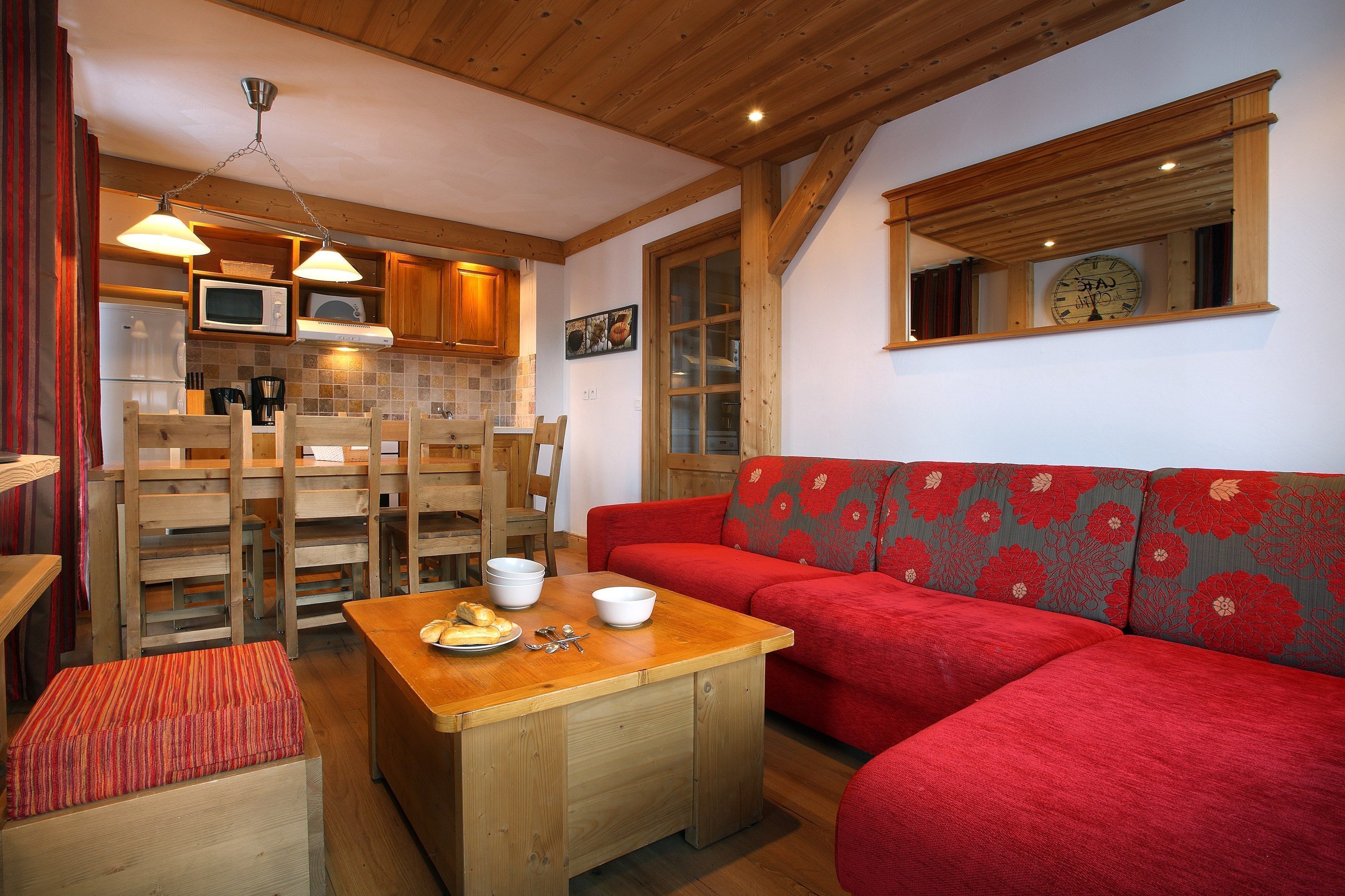 A cozy kitchen with wooden cabinets, a microwave, and a dining area with a red sofa and wooden table.