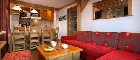 Cocina acogedora con armarios de madera, microondas y comedor con sofá rojo y mesa de madera.