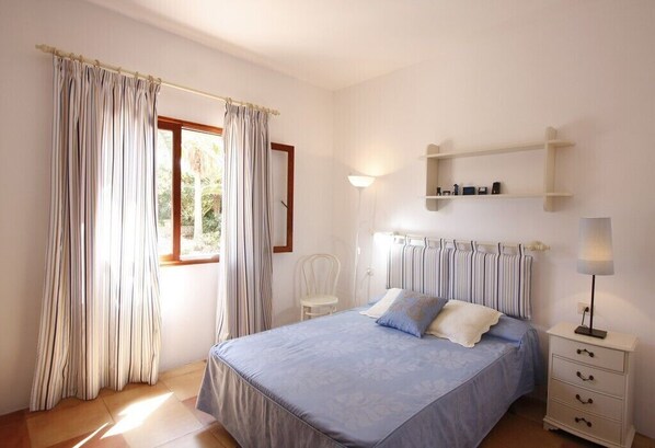 A bedroom with a bed, a chair, a bedside table, and a window with curtains.