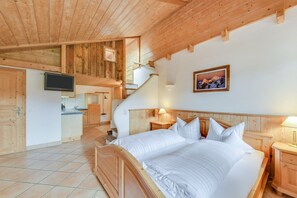 Une chambre avec un lit en bois, une télévision, un coin cuisine et un escalier.