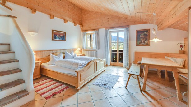 A bedroom with a wooden bed, a small table, a bench, a staircase, and a view through a glass door. - Cosy Apartment "Seekaralm" with Balcony, Garden & Wi-Fi (Lenggries)