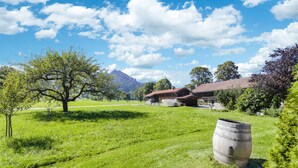 A rural landscape with a large tree, a wooden barrel, and a building with a red roof. - Cosy Apartment "Seekaralm" with Balcony, Garden & Wi-Fi (Lenggries)