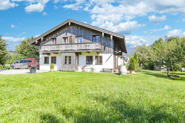 Une maison en bois à deux étages, dotée d’un balcon, entourée d’une pelouse bien entretenue et d’arbres.