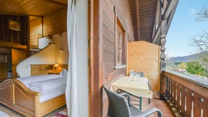 A wooden room with a bed, a table, and a chair, a staircase, and a view of the outdoors. - Cosy Apartment "Seekaralm" with Balcony, Garden & Wi-Fi (Lenggries)