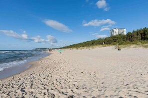 Ein weiter Sandstrand mit sanften Wellen, wolkenlosem Himmel und einem Gebäude im Hintergrund.