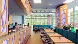 Un restaurante moderno con mesas de madera, asientos acolchados verdes, ventanas amplias y paneles decorativos en las paredes.