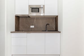 A compact kitchen with a built-in microwave, a sink, and a marble backsplash.