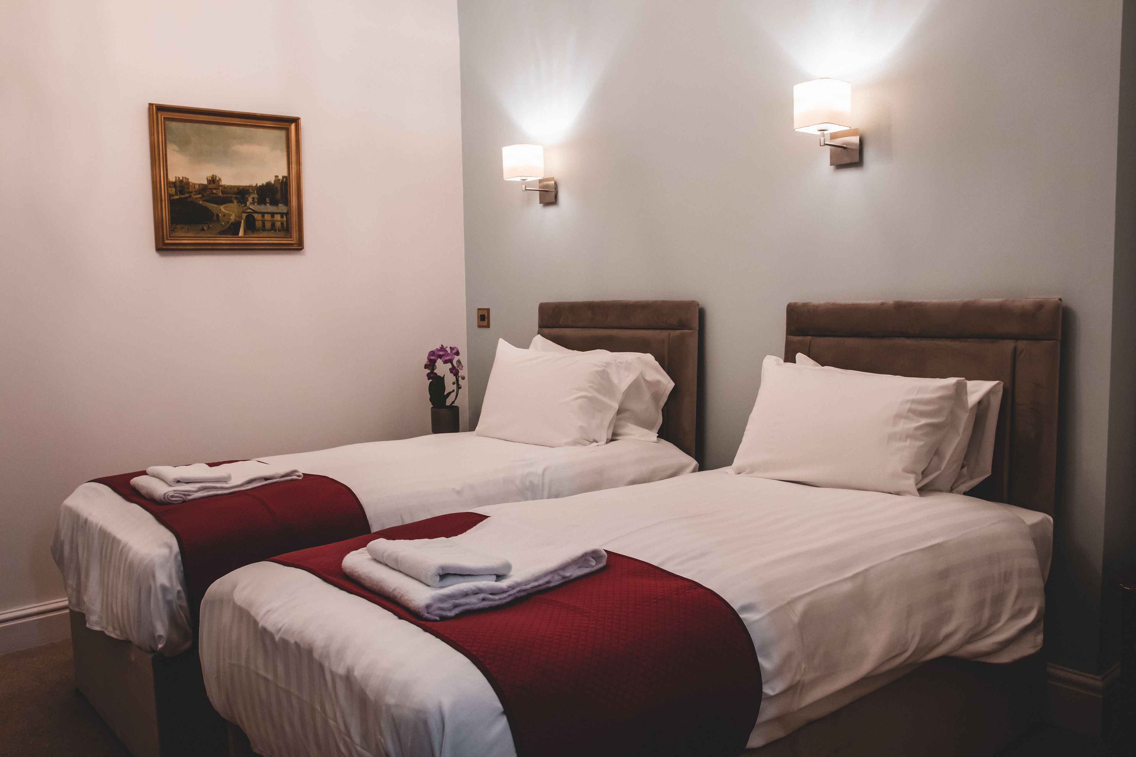 A hotel room with two beds, white bedding, red throw blankets, and a framed picture on the wall.