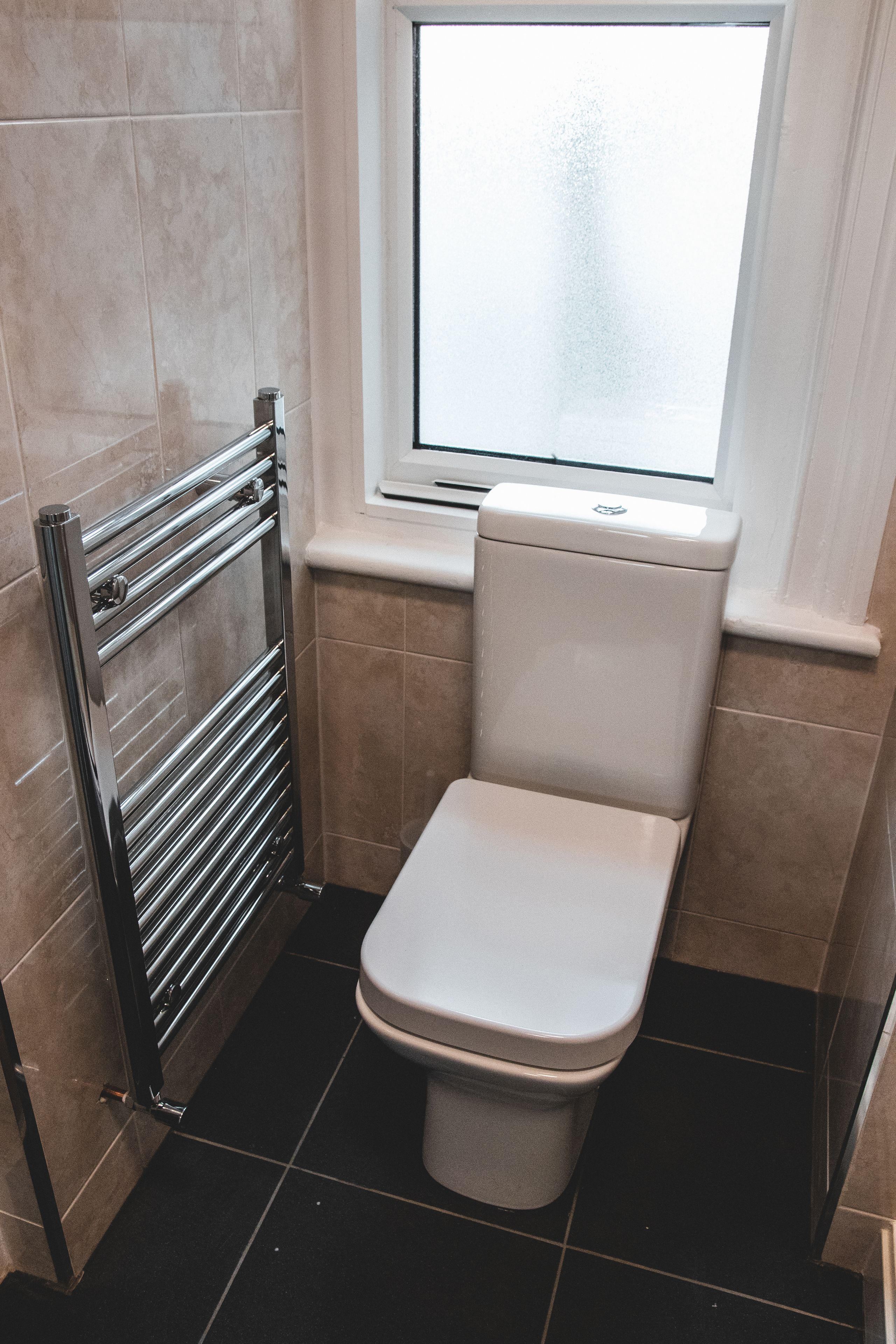 A small bathroom with a toilet, a towel rack, and a window.