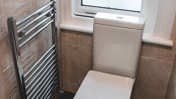 A small bathroom with a toilet, a towel rack, and a window.