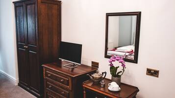 A room with a wooden dresser, a television on top, a small table with a teapot, cups, and a potted orchid.