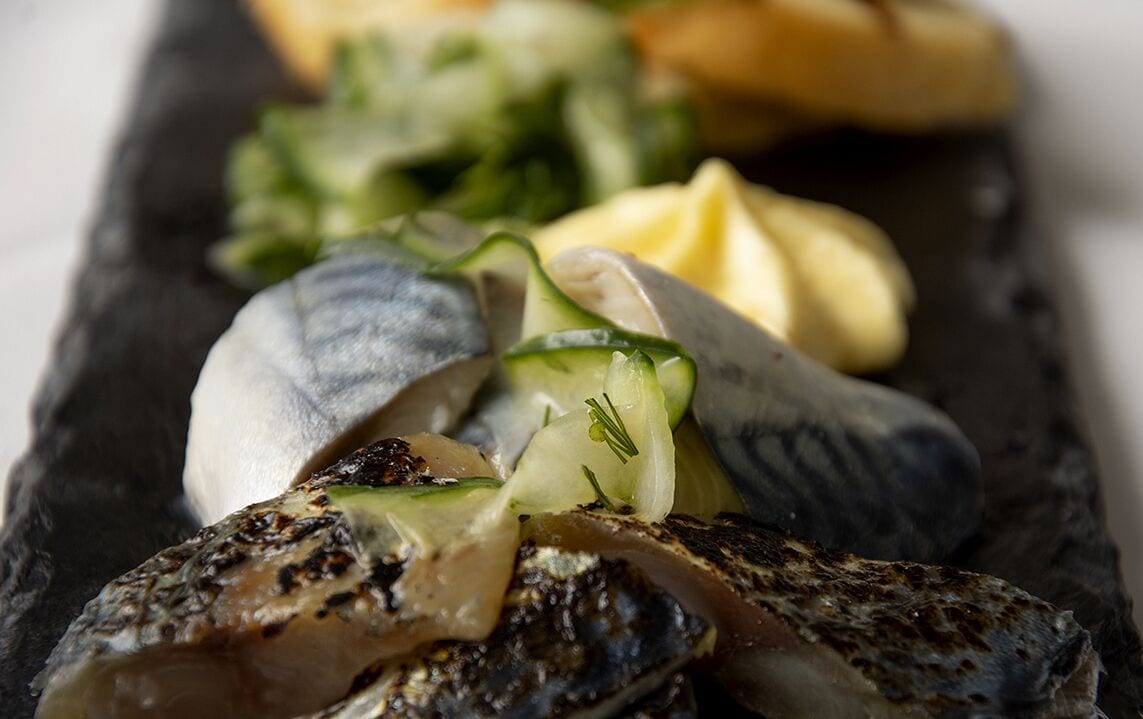 A close-up of a seafood dish with mussels and grilled fish on a slate plate.