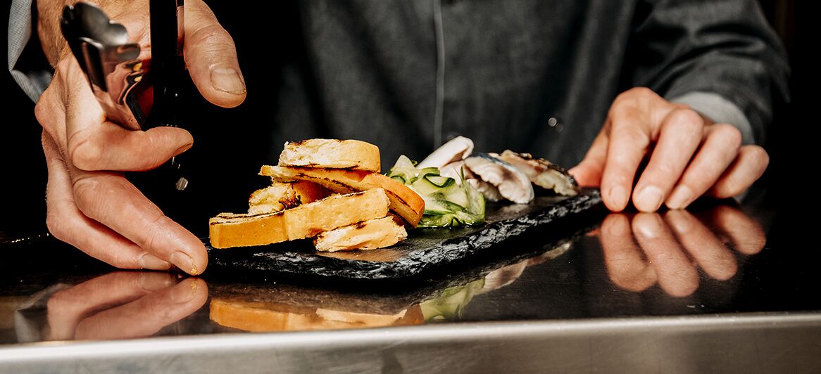 A person serving food on a black slate plate.