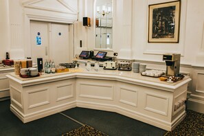 Un espace d’accueil d’hôtel avec un comptoir blanc incurvé, une machine à café et un tableau encadré accroché au mur.
