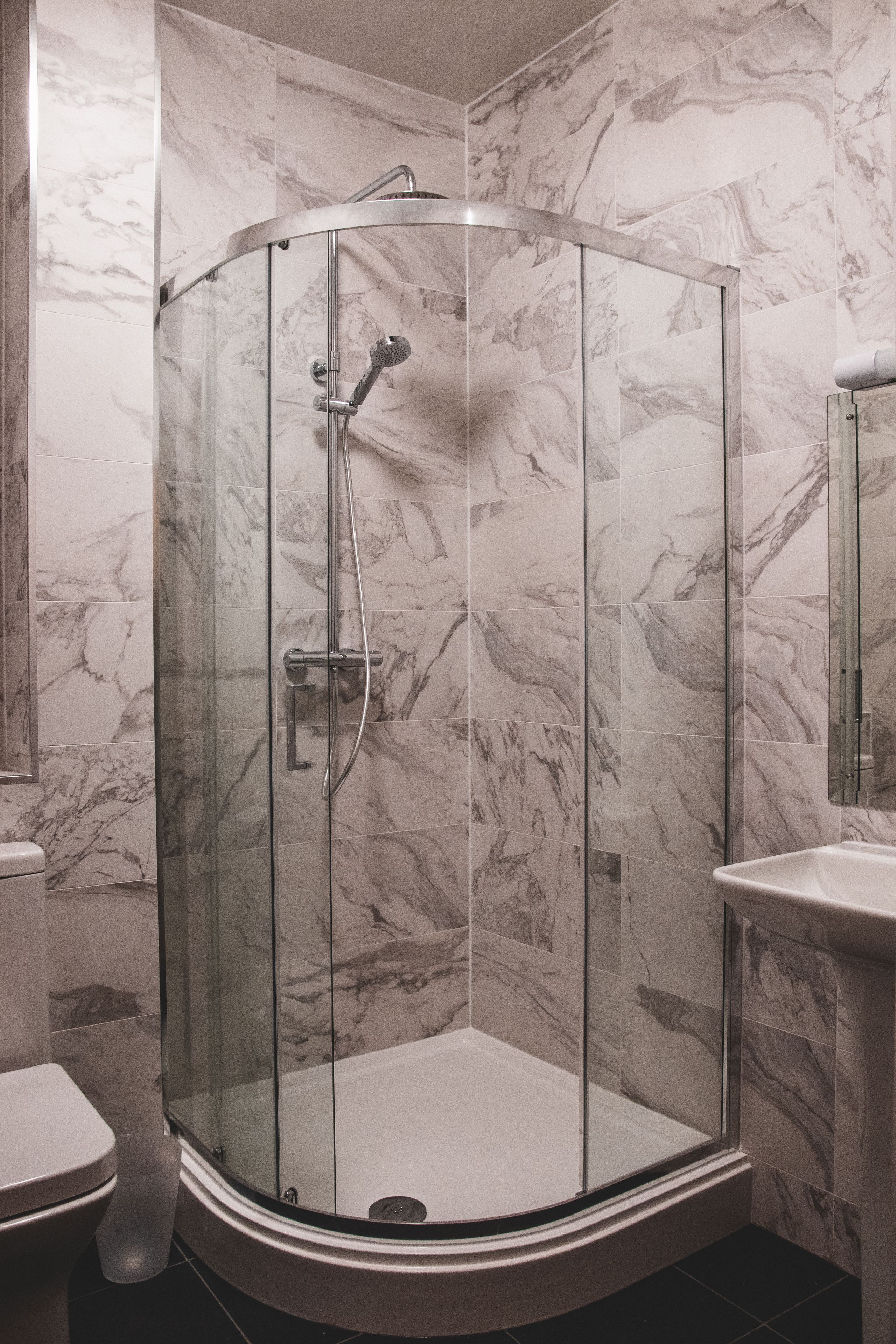 Ducha con paredes de diseño curvo y revestimiento de mármol, y una bañera blanca.