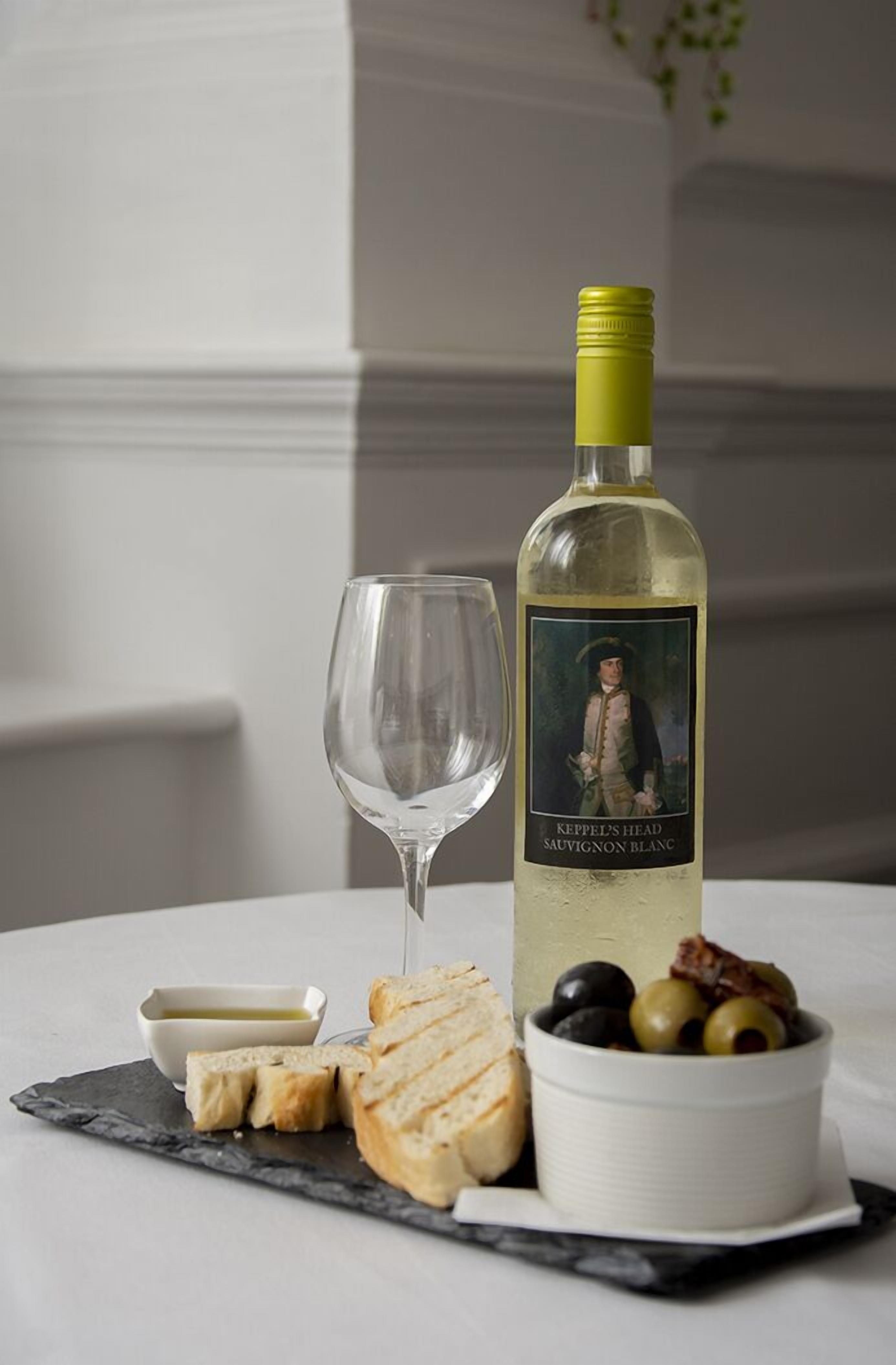 A bottle of Keppel's Head Sauvignon Blanc, a glass, sliced bread, olives, and a small bowl of butter on a marble table.