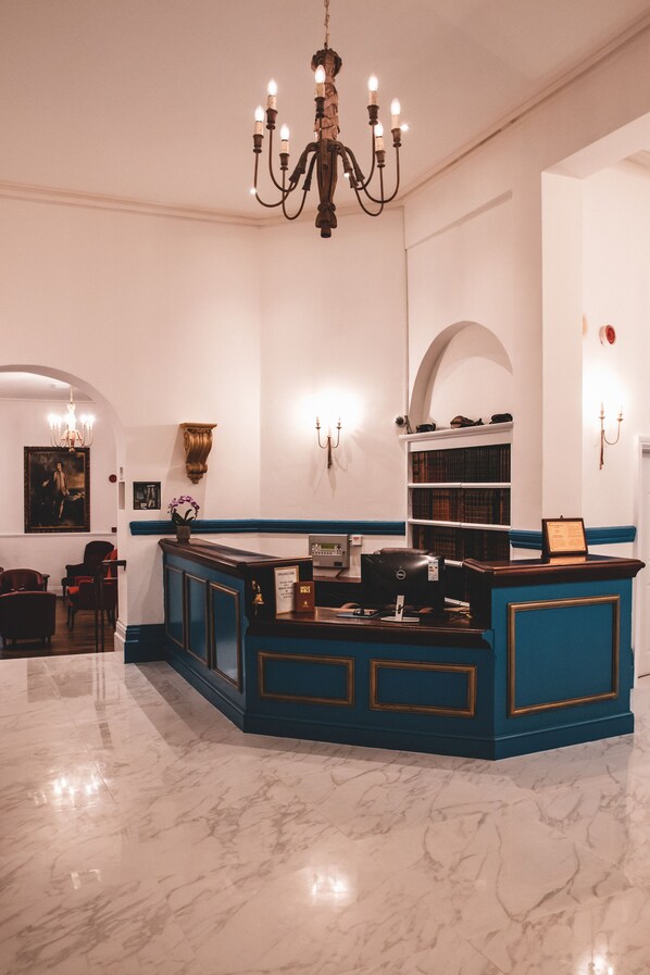 A reception area with a marble floor, a blue counter, a chandelier, and bookshelves. - Keppel's Head Hotel (Portsmouth)