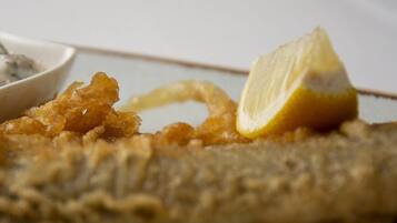 Un primo piano di un pesce fritto con una fetta di limone sopra, servito con una ciotola di salsa.