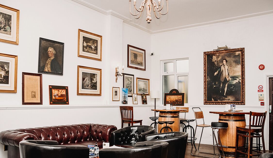 Una habitación con un sofá de cuero marrón, varias fotografías enmarcadas en la pared, una zona de bar de madera y un candelabro.