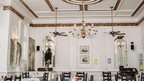 Ein formeller Speisesaal mit mehreren Tischen, edlen Kronleuchtern und klassischem Deckenstil.