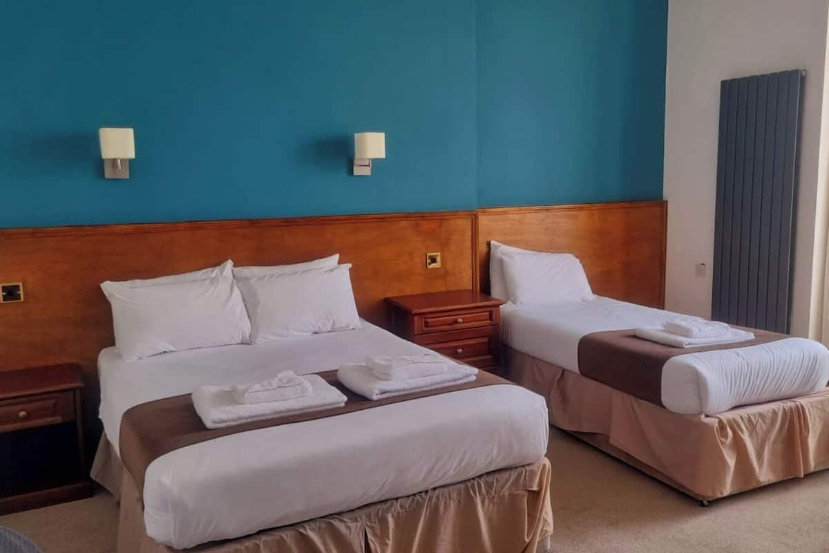 Hotellihuone, jossa on kaksi sänkyä, puinen pääty, valkoiset vuodevaatteet, puinen yöpöytä ja ikkuna, jossa on verhot.