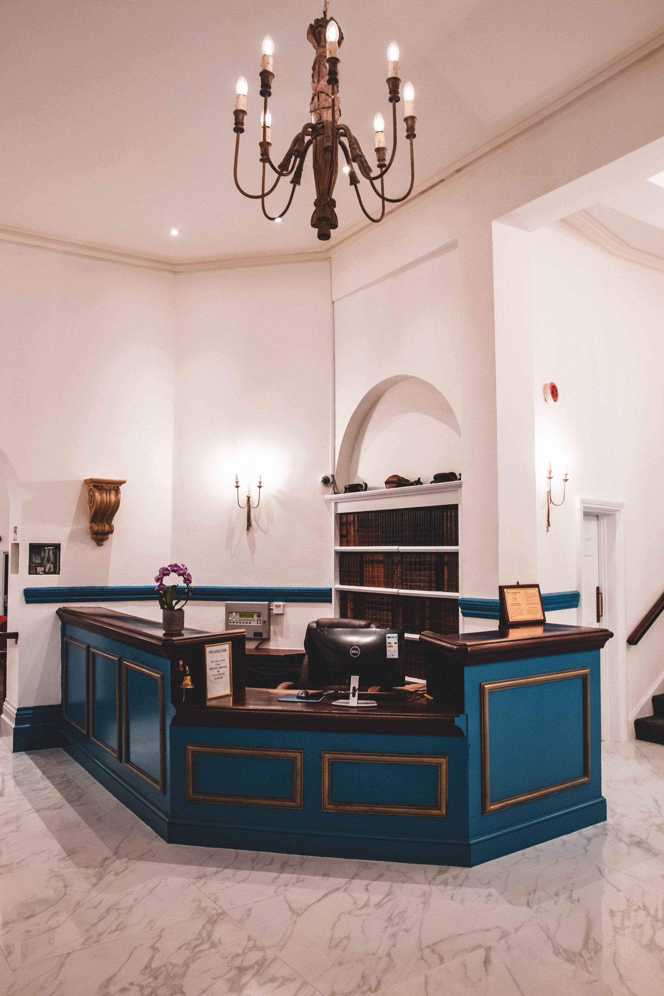 A reception area with a blue counter, a chandelier, bookshelves, and a staircase.