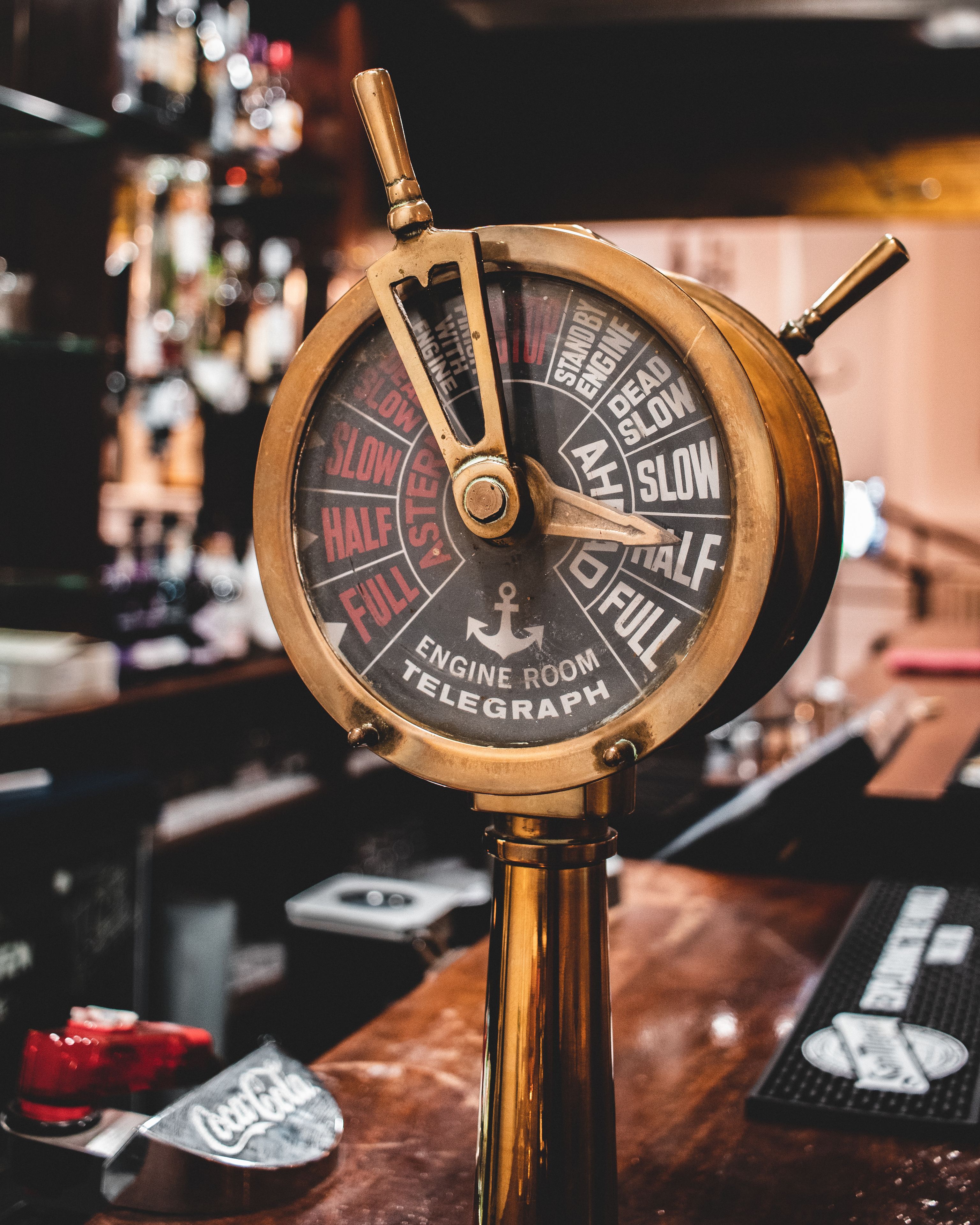 A brass ship's wheel with labels like "SLOW," "HALF," and "FULL" on a bar counter.