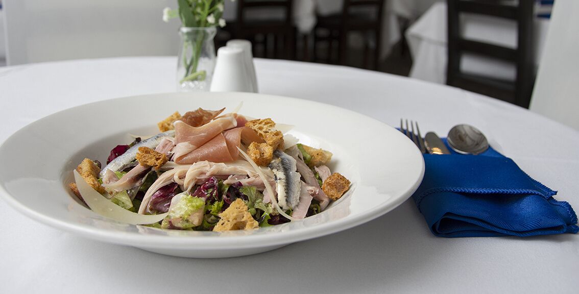 Een wit bord met een salade op een witte tafelkleed.