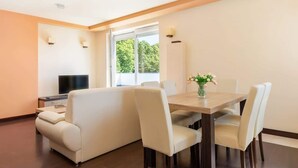 A dining area with a table and chairs, a sofa, a TV, and a window with a view of trees.