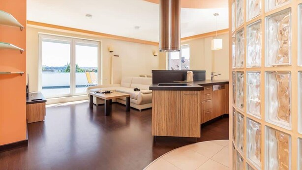 A modern living room with a kitchen area, a large window, and a view of the outdoors.